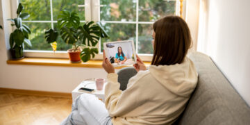 Image depicting a woman on the couch using her tablet for a virtual healthcare visit